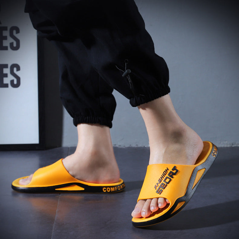 Person wearing yellow slides with black soles on a dark surface.