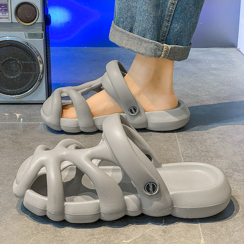 Gray sandals with unique strap design worn by a person, with a blue screen and speaker in the background.