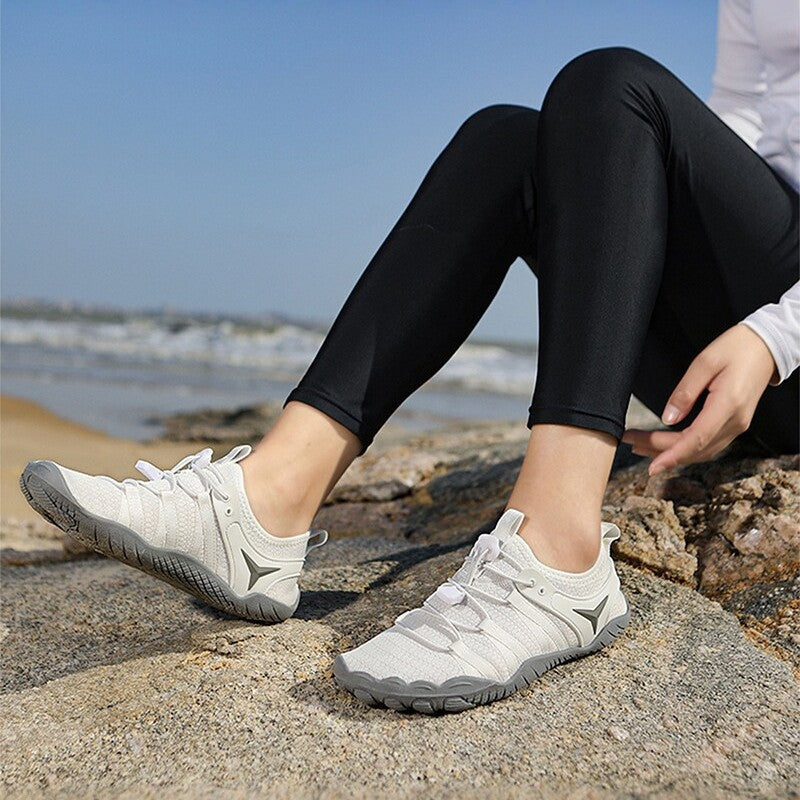 Person wearing white sneakers with a gray sole on a rocky surface by the water.