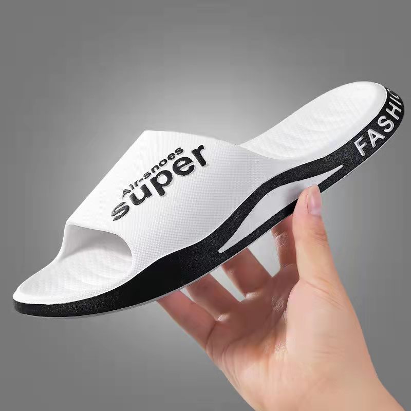 White slide sandal with black text held by a hand against a gray background
