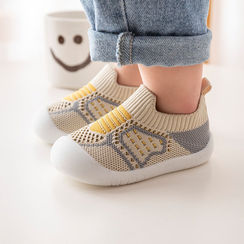 Children's beige and gray shoes with yellow accents worn by a child.