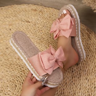 Pink sandals with large bows held by a hand on a woven surface