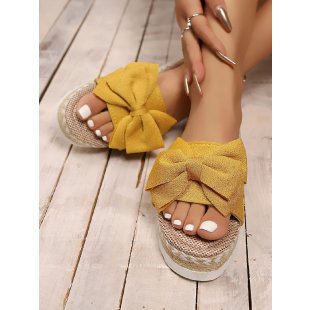 Yellow sandals with ruffled straps worn on a wooden floor