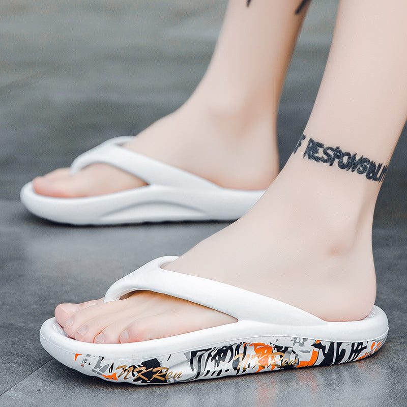 White flip-flops with colorful patterns worn by a person on a gray surface.
