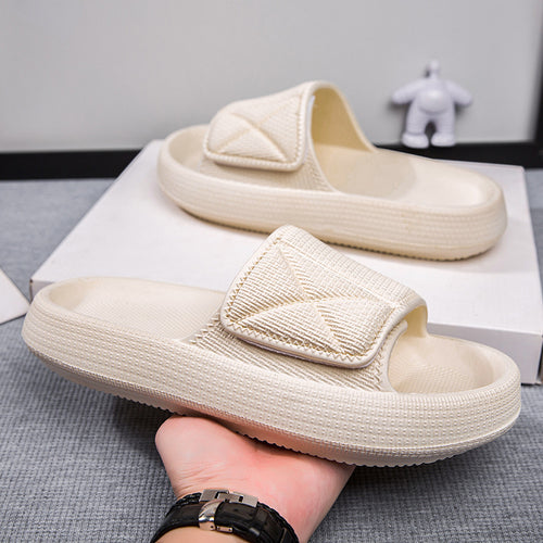 Beige slippers being held by a hand on a gray surface with a white box in the background.